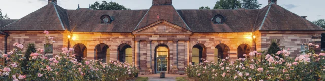 Vue extérieure du bâtiment des thermes de Luxeuil-les-Bains à la tombée de la nuit, construit en grès rose des Vosges et dont l'allée est bordée de rosiers - Vosges du Sud