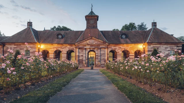 Vue extérieure du bâtiment des thermes de Luxeuil-les-Bains à la tombée de la nuit, construit en grès rose des Vosges et dont l'allée est bordée de rosiers - Vosges du Sud