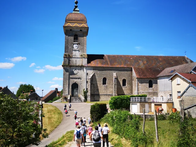 Un groupe de randonneurs se dirigent vers une église au clocher comtois et tuiles vernissées, typique de la Franche-Comté - Vallée de l'Ognon