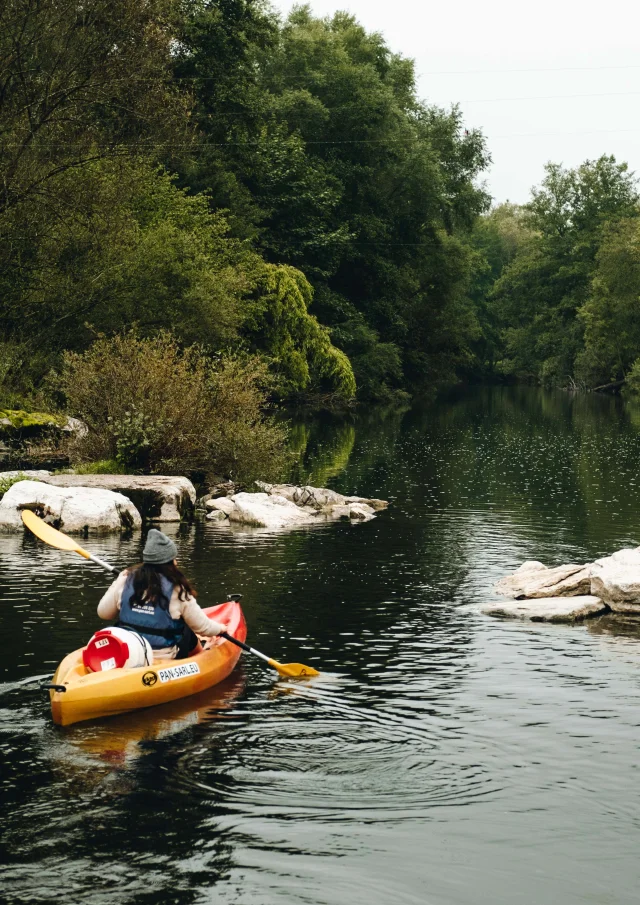 A l'automne, une femme descend la rivière Ognon en canoë et une vache l'observe en arrière-plan - Vallée de l'Ognon