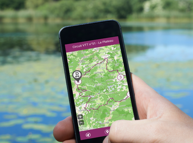 Une personne tient un smartphone avec l'application My Haute-Saône ouverte, permettant de suivre un itinéraire VTT en direct