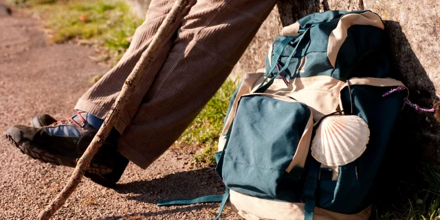 Un pèlerin fait une pause avec à ses pieds, son sac de randonnée sur lequel on voit la coquille, symbole de Compostelle