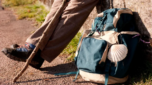 Un pèlerin fait une pause avec à ses pieds, son sac de randonnée sur lequel on voit la coquille, symbole de Compostelle