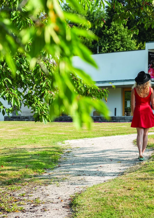 Une femme avec une robe rouge se promène dans les cerisiers devant l'écomusée du Pays de la Cerise - Fougerolles - Vosges du Sud