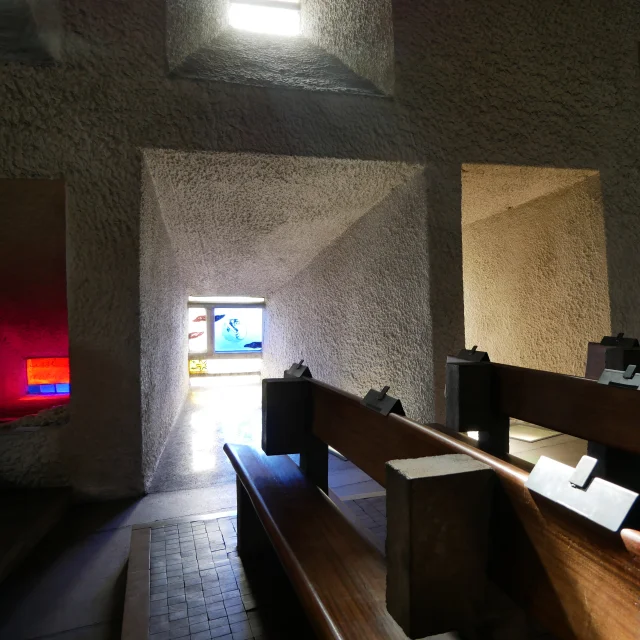 Intérieur de la chapelle Notre-Dame du Haut, où on retrouve des bancs en bois, des vitraux qui font des puits de lumières colorés - Peint par Le Corbusier - site UNESCO - Vosges du Sud