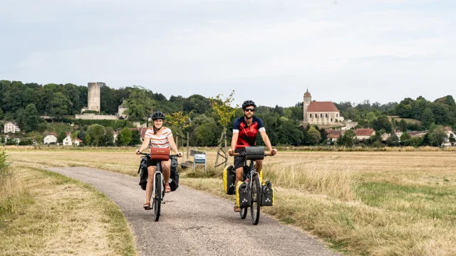 Un couple de cyclistes pédale sur La Voie Bleue, le long de la Saône avec le château de Rupt-sur-Saône en arrière-plan - Vesoul-Val de Saône