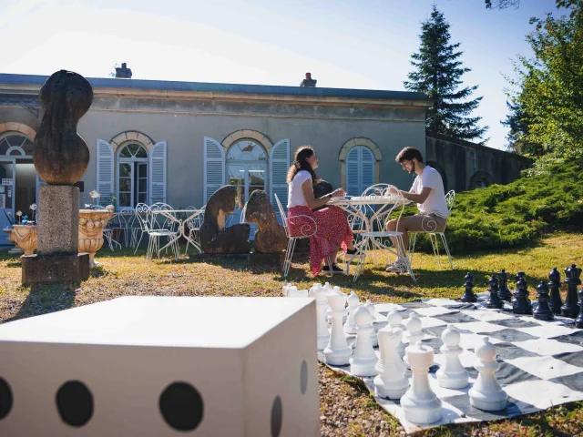 Un couple déjeune en terrasse au Musée Baron Martin. Au premier-plan, on voit un jeu d'échec de grande taille - Gray - Cité de caractère - Vesoul - Val de Saône