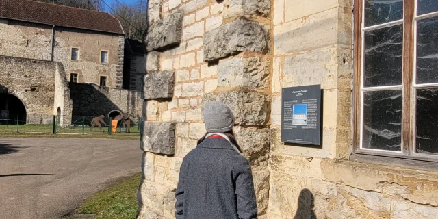 Une femme lit un panneau de médiation qui est fixé au mur des Forges de Baignes - logement ouvrier - Vesoul - Val de Saône