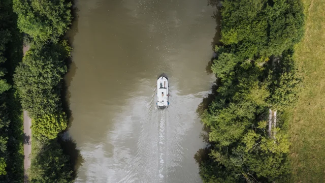 Vue aérienne d'un bateau sans permis navigant sur la Saône, dans un cadre de nature préservée, au milieu de la verdure - Vesoul-Val de Saône