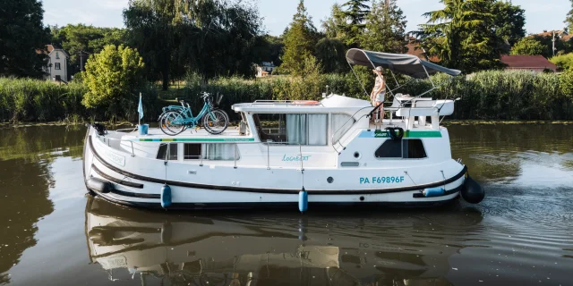 Un femme pilote un bateau sans permis sur la Saône, en admirant le paysage alentour, en pleine nature préservée - Vesoul-Val de Saône