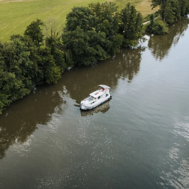 Vue aérienne d'un bateau sans permis navigant sur la Saône, dans un cadre de nature préservée, au milieu de la verdure - Vesoul-Val de Saône