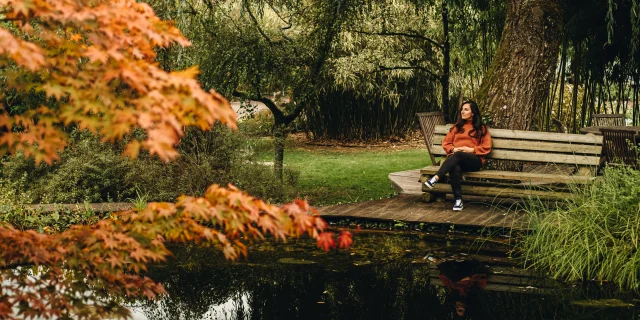 Une femme assise sur un bans au bord d'un bassin des jardins aquatiques Acorus rêvasse - Vallée de l'Ognon