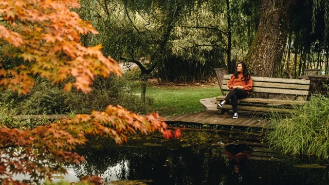 Une femme assise sur un bans au bord d'un bassin des jardins aquatiques Acorus rêvasse - Vallée de l'Ognon