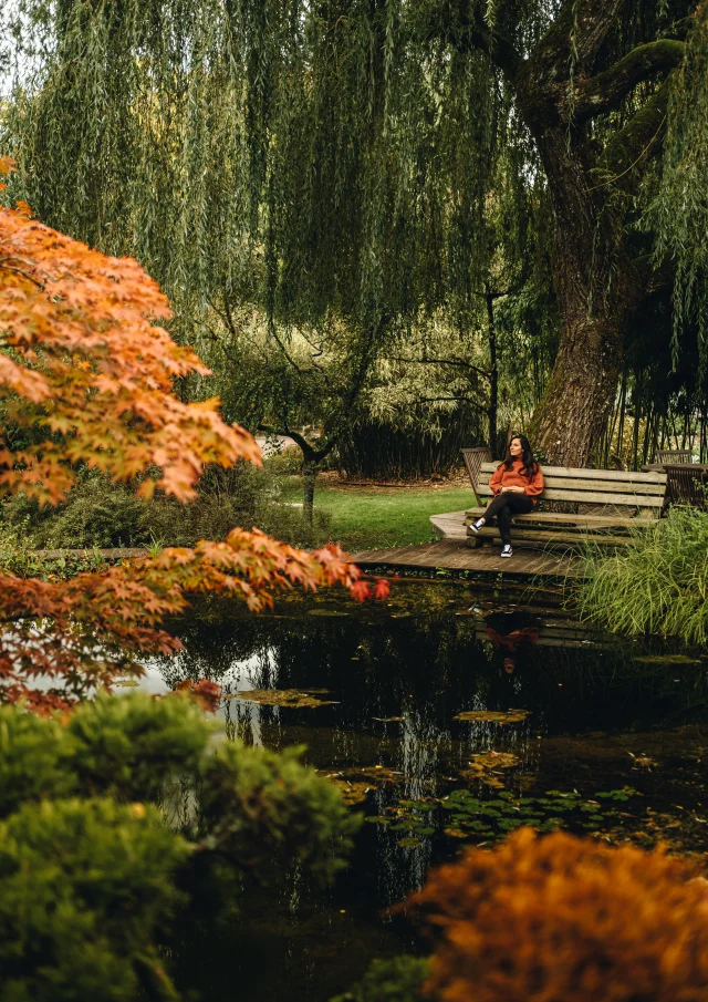 Une femme assise sur un bans au bord d'un bassin des jardins aquatiques Acorus rêvasse - Vallée de l'Ognon