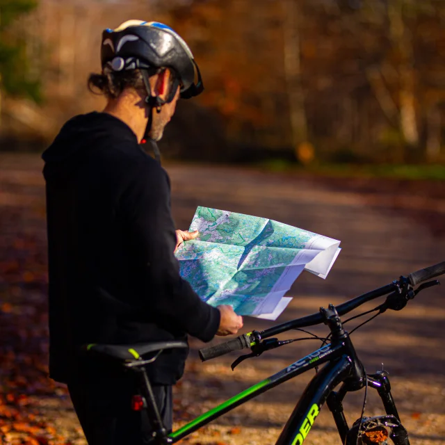 Un VTTiste consulte une carte de son parcours dans une forêt aux couleurs automnales - Vosges du Sud