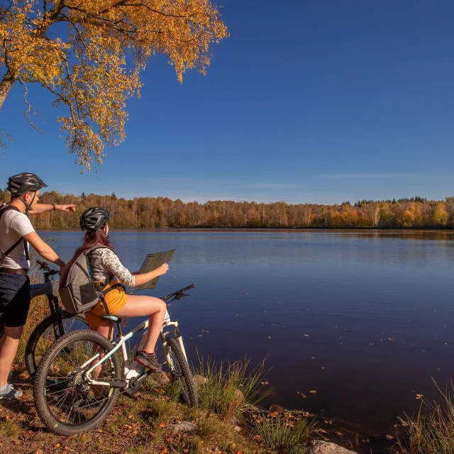 Un couple en VTT fiat une pause au bord d'un étang, avec des couleurs automnales, sur le Plateau des 1000 Etangs - Vosges du Sud