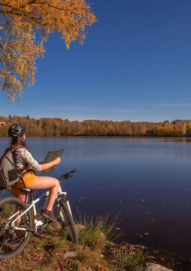 Un couple en VTT fiat une pause au bord d'un étang, avec des couleurs automnales, sur le Plateau des 1000 Etangs - Vosges du Sud