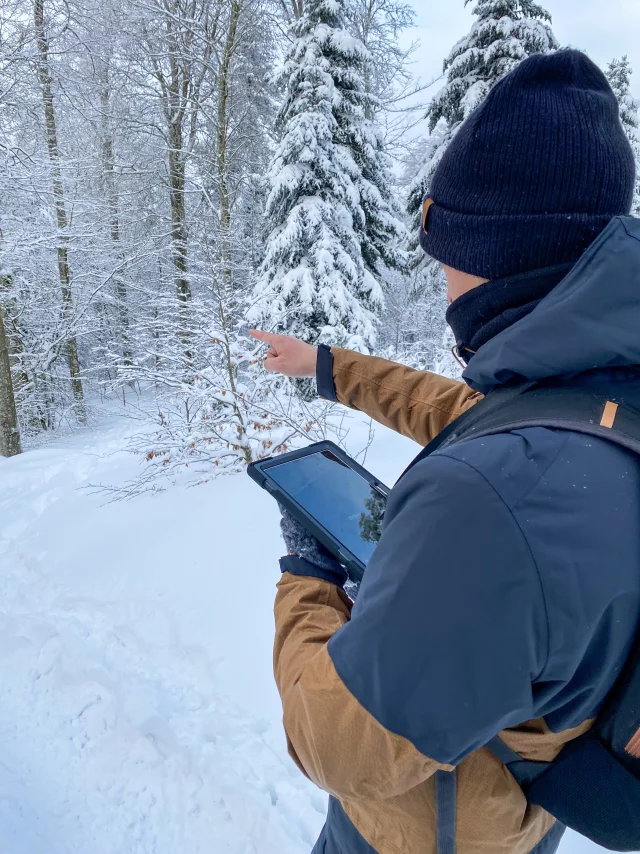 Un homme tient une tablette pour jouer à l'Explor Game de La planche des Belles Filles, au milieu d'un paysage enneigé - Vosges du Sud