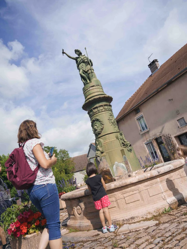 Une famille visite Jussey, grâce à l'application Baludik - On aperçoit une fontaine avec une statue de femme - Vesoul - Val de Saône