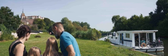 Une famille est en bord de Saône, on aperçoit un bateau de plaisance, en arrière-plan il y a le château de Ray-sur-Saône - Vesoul - Val de Saône