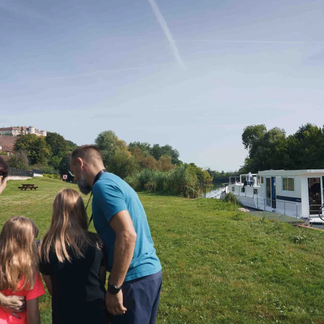 Une famille est en bord de Saône, on aperçoit un bateau de plaisance, en arrière-plan il y a le château de Ray-sur-Saône - Vesoul - Val de Saône