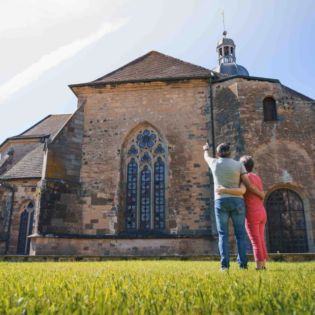 Un couple regarde l'église abbatiale de Faverney. L'homme pointe du doigt le clocher - Vesoul - Val de Saône