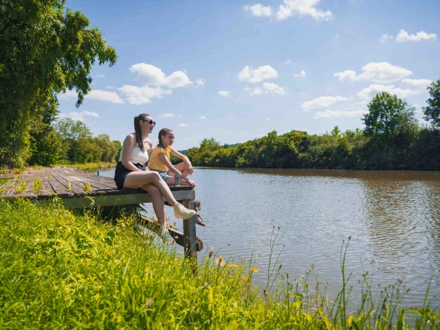 Deux jeunes filles sont assises sur un ponton le long de la Saône à Port sur Saône. Elles profitent du paysage - Vesoul - Val de Saône