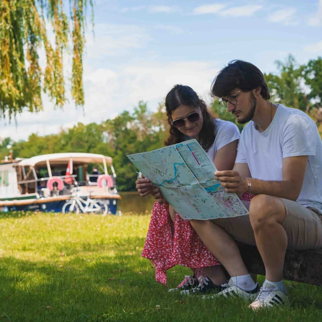 Un couple, en bord de Saône, regarde un plan de la Ville de Gray - Derrière eux, on retrouve des bateaux et un vélo - Gray - Vesoul - Val de Saône