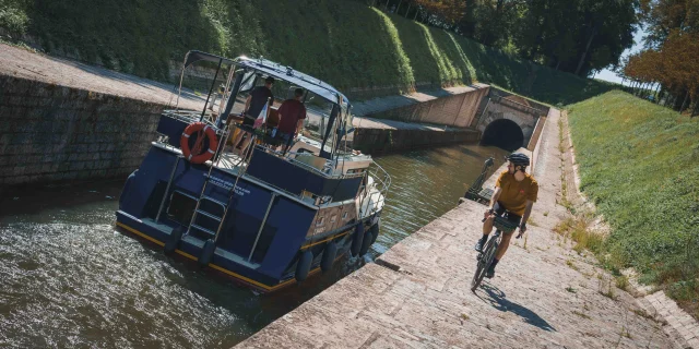 Un bateau s'apprête à rentrer dans le tunnel de Saint-Albin, sur le côté un cycliste itinérant regarde le bateau - Vesoul - Val de Saône