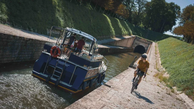 Un bateau s'apprête à rentrer dans le tunnel de Saint-Albin, sur le côté un cycliste itinérant regarde le bateau - Vesoul - Val de Saône