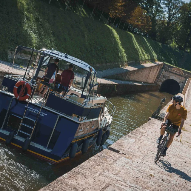 Un bateau s'apprête à rentrer dans le tunnel de Saint-Albin, sur le côté un cycliste itinérant regarde le bateau - Vesoul - Val de Saône