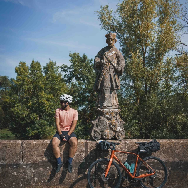 Un cycliste emprunte la Trace du Courlis qui permet de faire la liaison entre la V50 et l'EV6. Il fait une pause sur un mur où se trouve une statue en pierre - Vesoul - Val de Saône