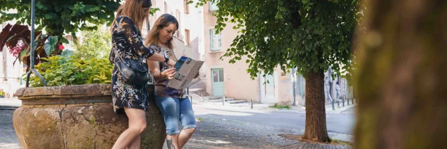 Deux femmes consultent une carte touristique, appuyées sur un puits, sur une place de la ville de Vesoul - Vesoul-Val de Saône