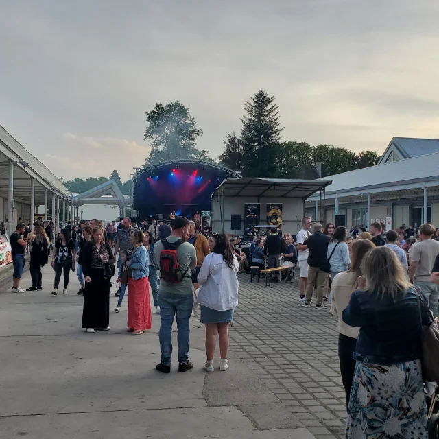 Le public profite de l'ambiance et des stands du ROAFF festival pendant qu'un groupe joue sur la scène en arrière plan - Festival de musique ROAFF à la Filature de Ronchamp - Vosges du Sud