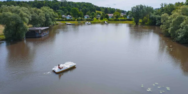 Un bateau navigue sur la Saône, il s'approche du Domaine Saône Valley. On voit l'hébergement flottant ainsi que les petits chalets - Vesoul - Val de Saône