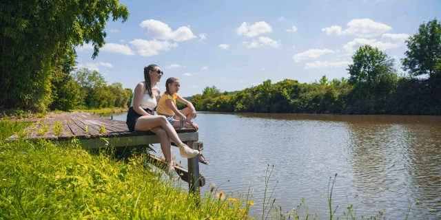 Deux jeunes filles sont assises sur un ponton le long de la Saône à Port sur Saône. Elles profitent du paysage - Vesoul - Val de Saône