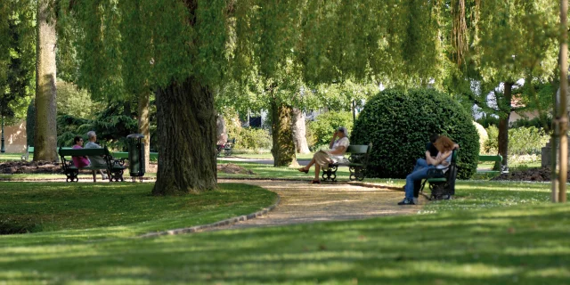 De nombreuses personnes sont assises sur des bancs et profitent de l'ombre au Jardin Anglais de Vesoul - Vesoul - Val de Saône