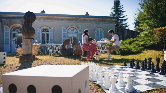 Un couple déjeune en terrasse au Musée Baron Martin. Au premier-plan, on voit un jeu d'échec de grande taille - Gray - Cité de caractère - Vesoul - Val de Saône