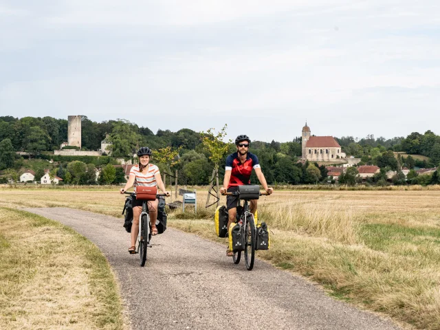 Un couple de cyclistes pédale sur La Voie Bleue, le long de la Saône avec le château de Rupt-sur-Saône en arrière-plan - Vesoul-Val de Saône