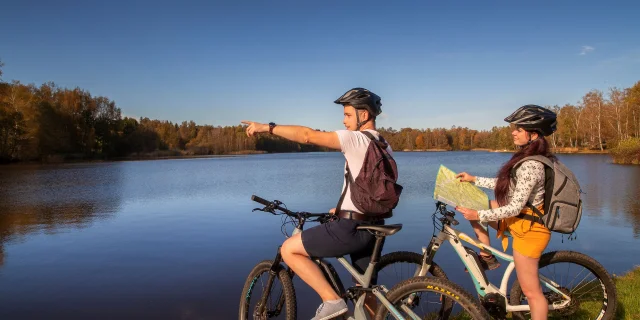 Un couple en VTT fiat une pause au bord d'un étang, avec des couleurs automnales, sur le Plateau des 1000 Etangs - Vosges du Sud