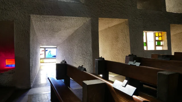 Intérieur de la chapelle Notre-Dame du Haut, où on retrouve des bancs en bois, des vitraux qui font des puits de lumières colorés - Peint par Le Corbusier - site UNESCO - Vosges du Sud