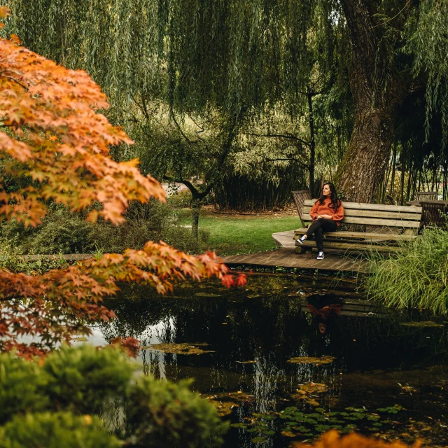 Une femme assise sur un bans au bord d'un bassin des jardins aquatiques Acorus rêvasse - Vallée de l'Ognon