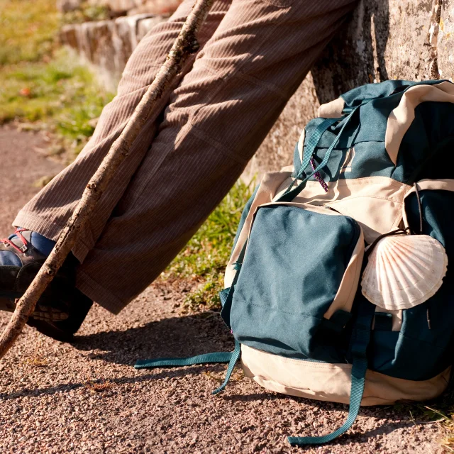 Un pèlerin fait une pause avec à ses pieds, son sac de randonnée sur lequel on voit la coquille, symbole de Compostelle