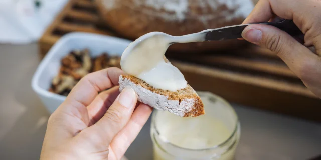 Une femme étale de la cancoillotte IGP sur un morceau de pain, cancoillotte fabriquée par la fromagerie bio La Fleurizelle à Aboncourt-Gesincourt - Vesoul-Val de Saône