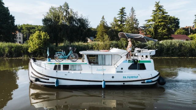 Un femme pilote un bateau sans permis sur la Saône, en admirant le paysage alentour, en pleine nature préservée - Vesoul-Val de Saône