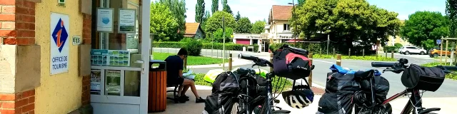 Des touristes ont garé leur vélo pendant qu’une personne consulte une carte devant l'office de tourisme de la Cité de Caractère de Villersexel - Vallée de l'Ognon